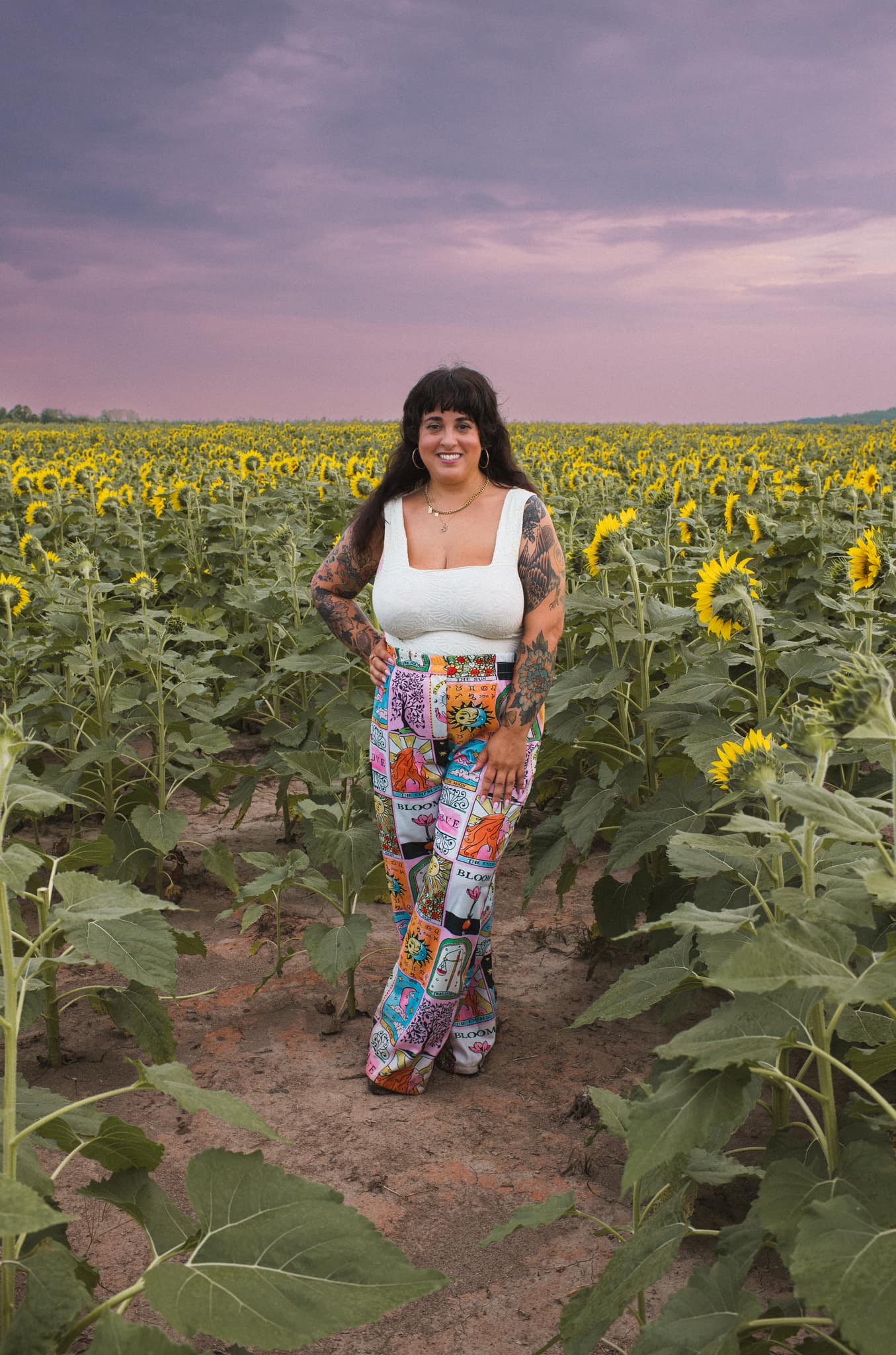 J.J. standing on a path through a sunflower field under a violet sky.