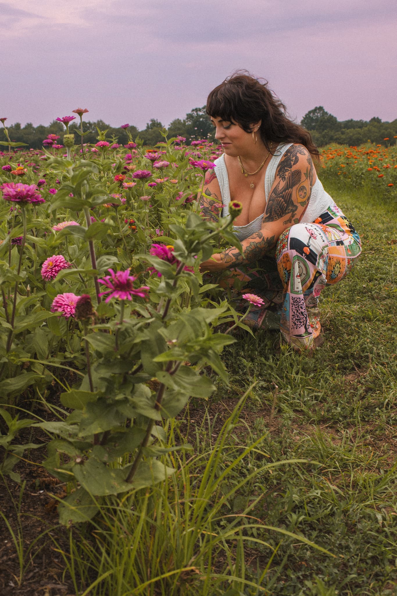 J.J. kneeling in a zinnia field at dusk, tending the pink blooms in front of her.