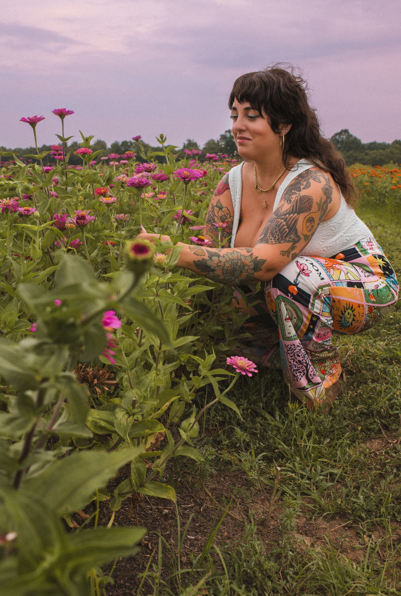 J.J. reaching out to a single zinnia in a flower field under a lavender evening sky.