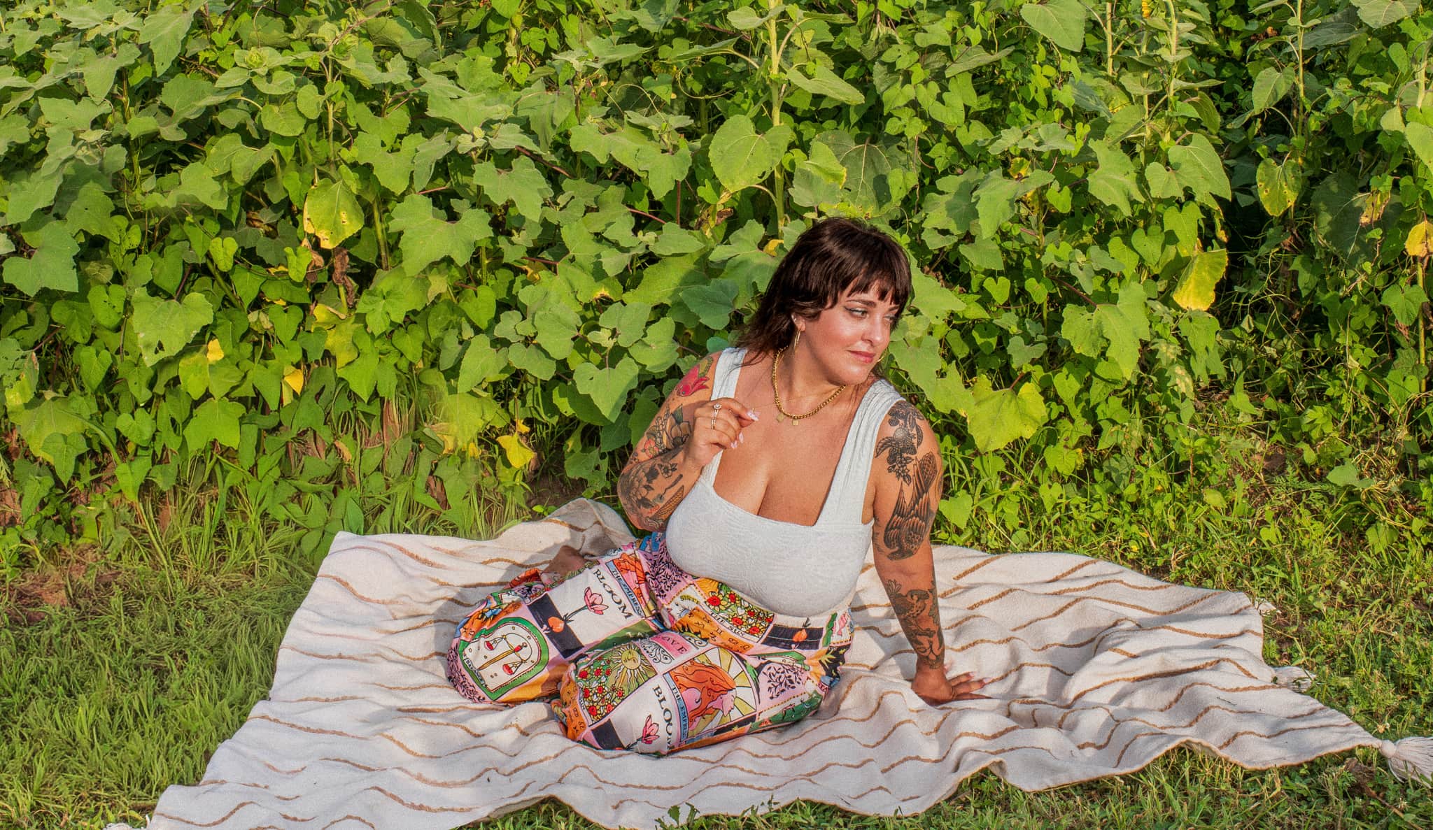 J.J. seated on a blanket in front of dense green foliage.