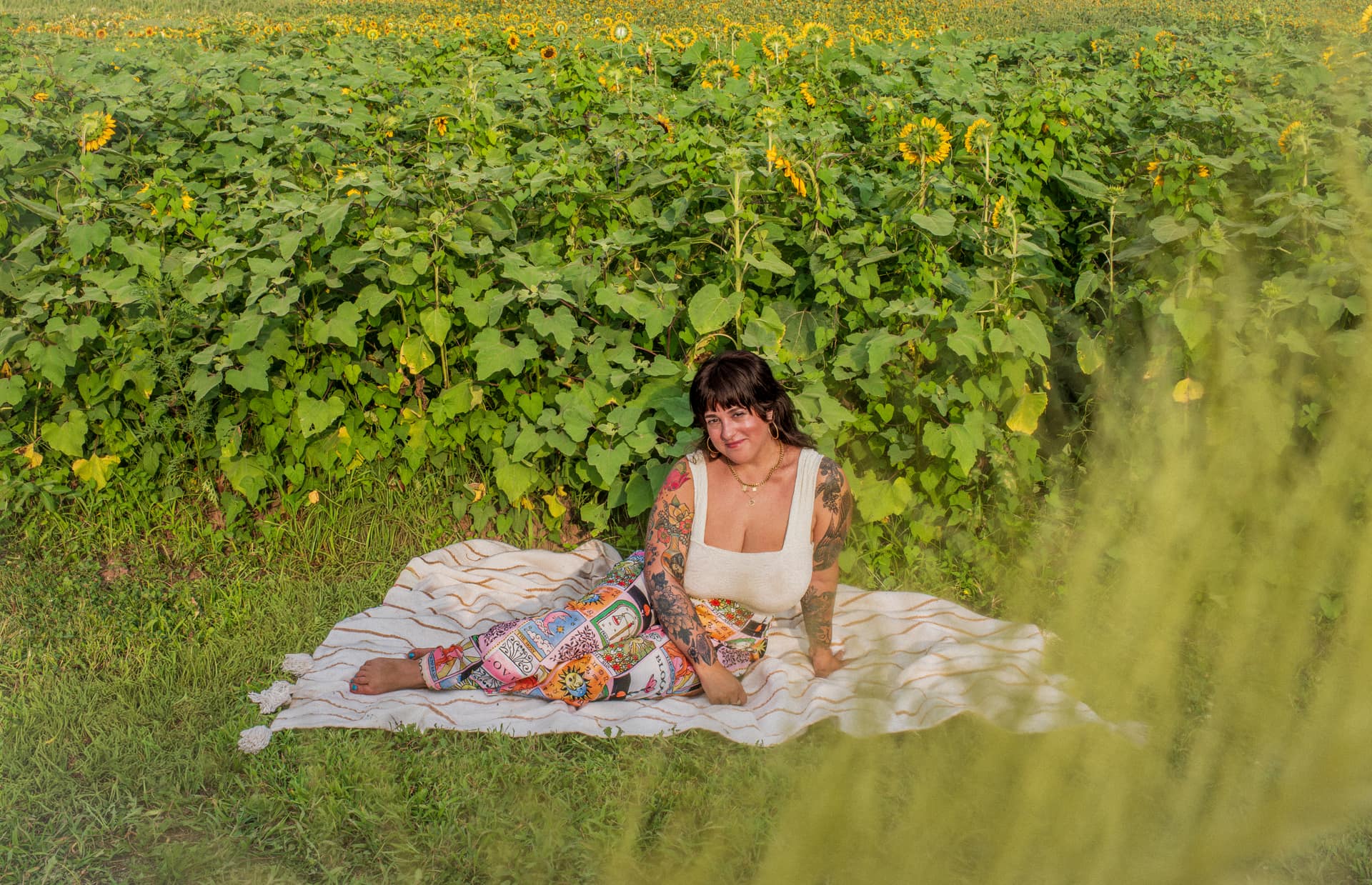 J.J. seated on a blanket in front of a wall of tall sunflowers.